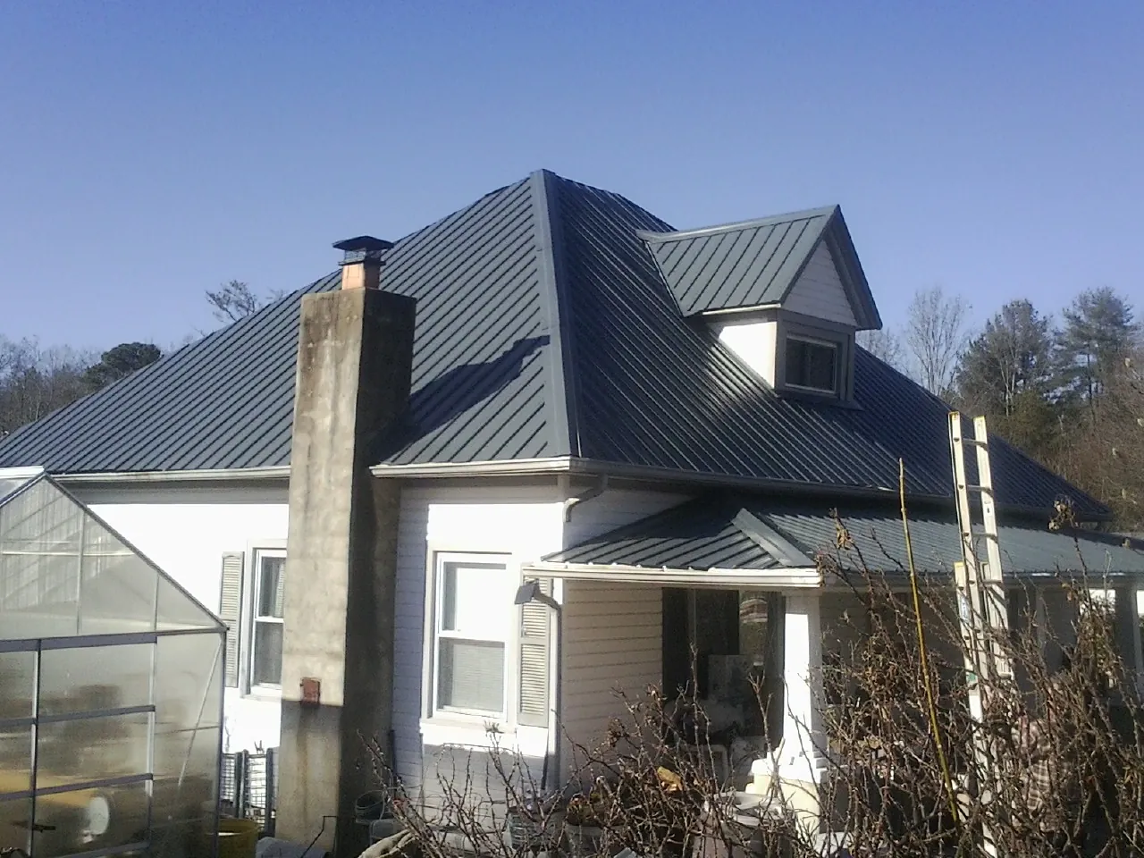 Dark blue standing seam metal roof on a white farmhouse with dormer — Slate & Tile Roof Repair by Roofing Brothers in Minot