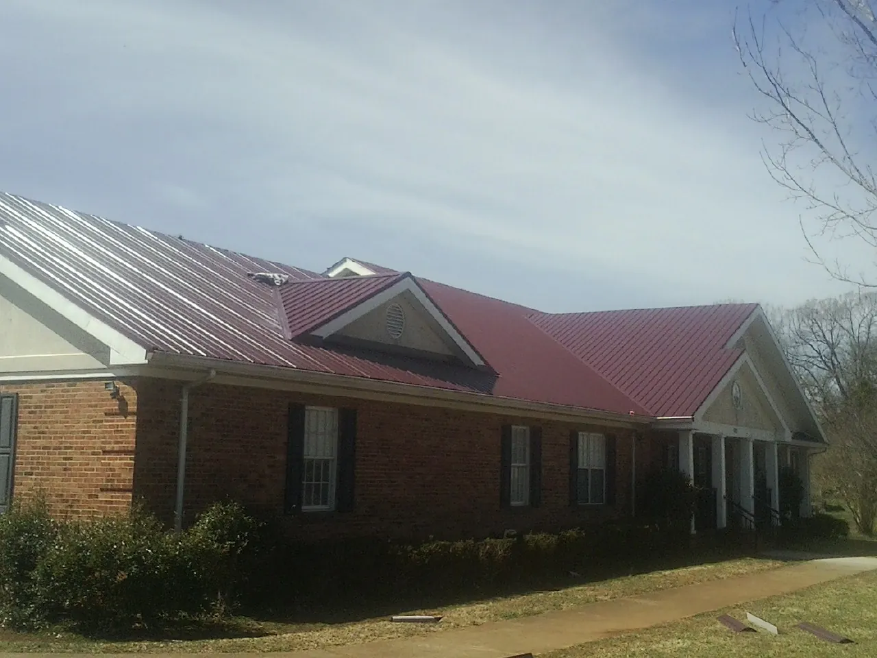 Red metal roof with gabled entries on a long brick building, from a Hail Damage Roof Repair job in Minot