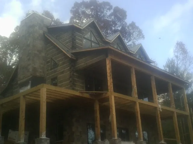 Stone chimney and dormers on a large log home with a timber porch in Minot