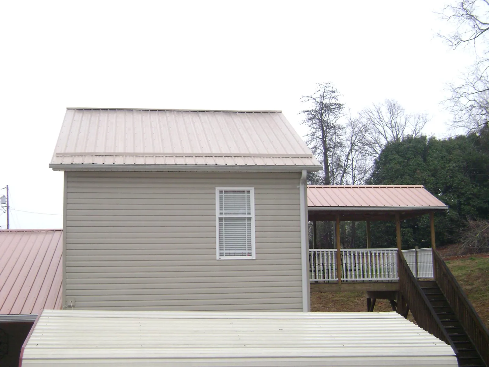Tan metal roofs on a two story addition and attached porch, from a Roof Replacement job in Minot